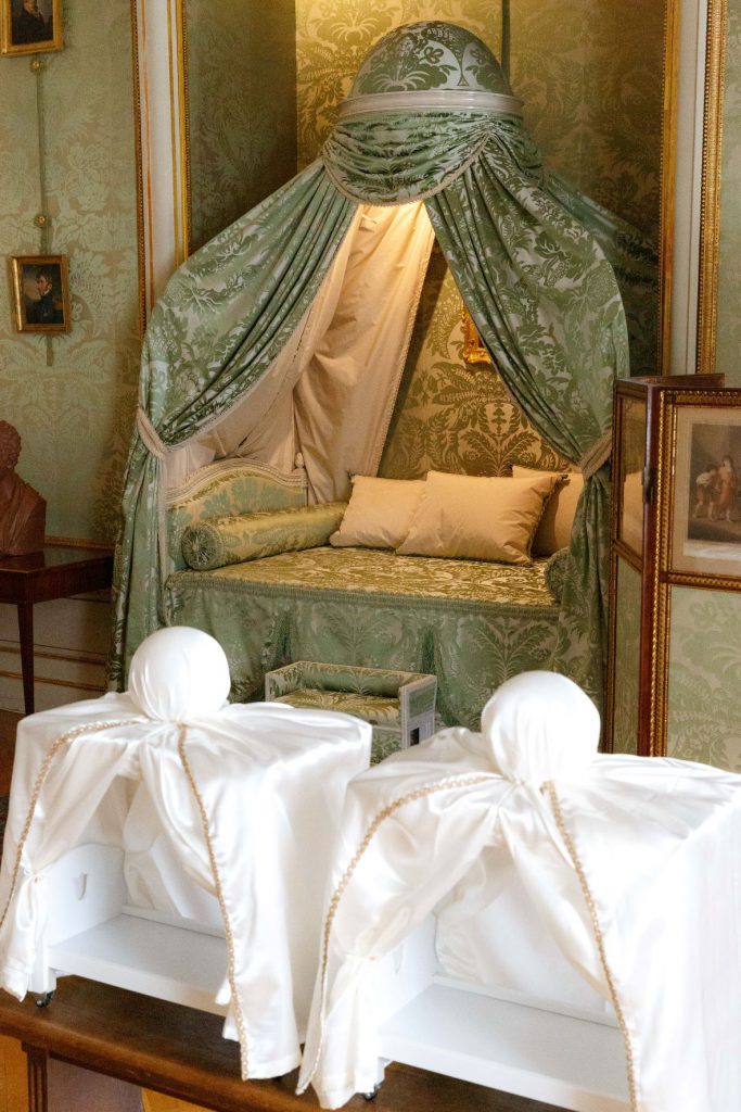  Zdjęcie wykonane w Muzeum w Nieborowie i Arkadii. Kadr pionowy. Na pierwszym planie miniaturowe modele łóżka à la polonaise. W tle oryginalne łóżko eksponowane w sypialni wojewody w Pałacu w Nieborowie. 